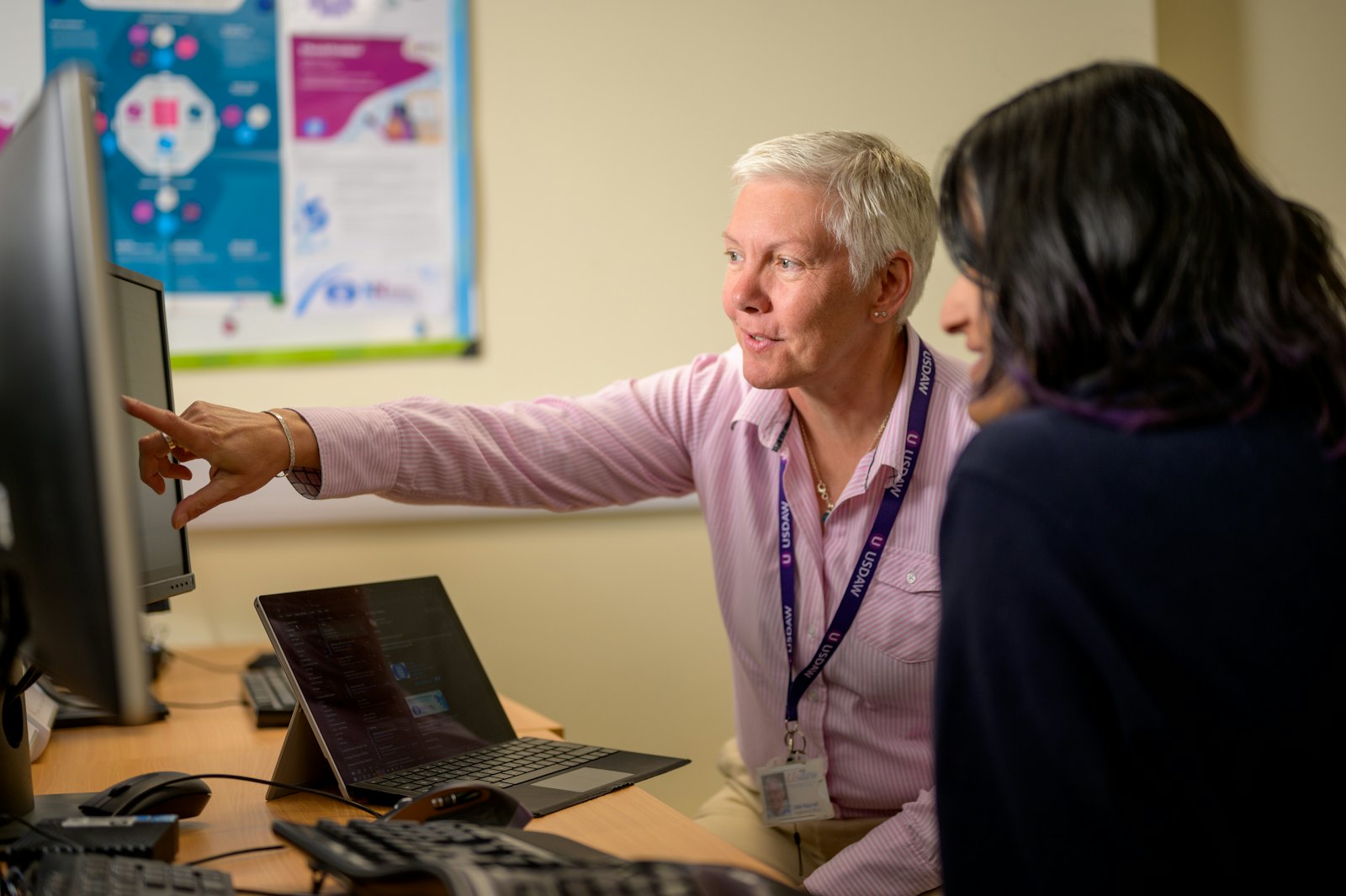 An IT support person pointing at a computer screen while helping a colleague