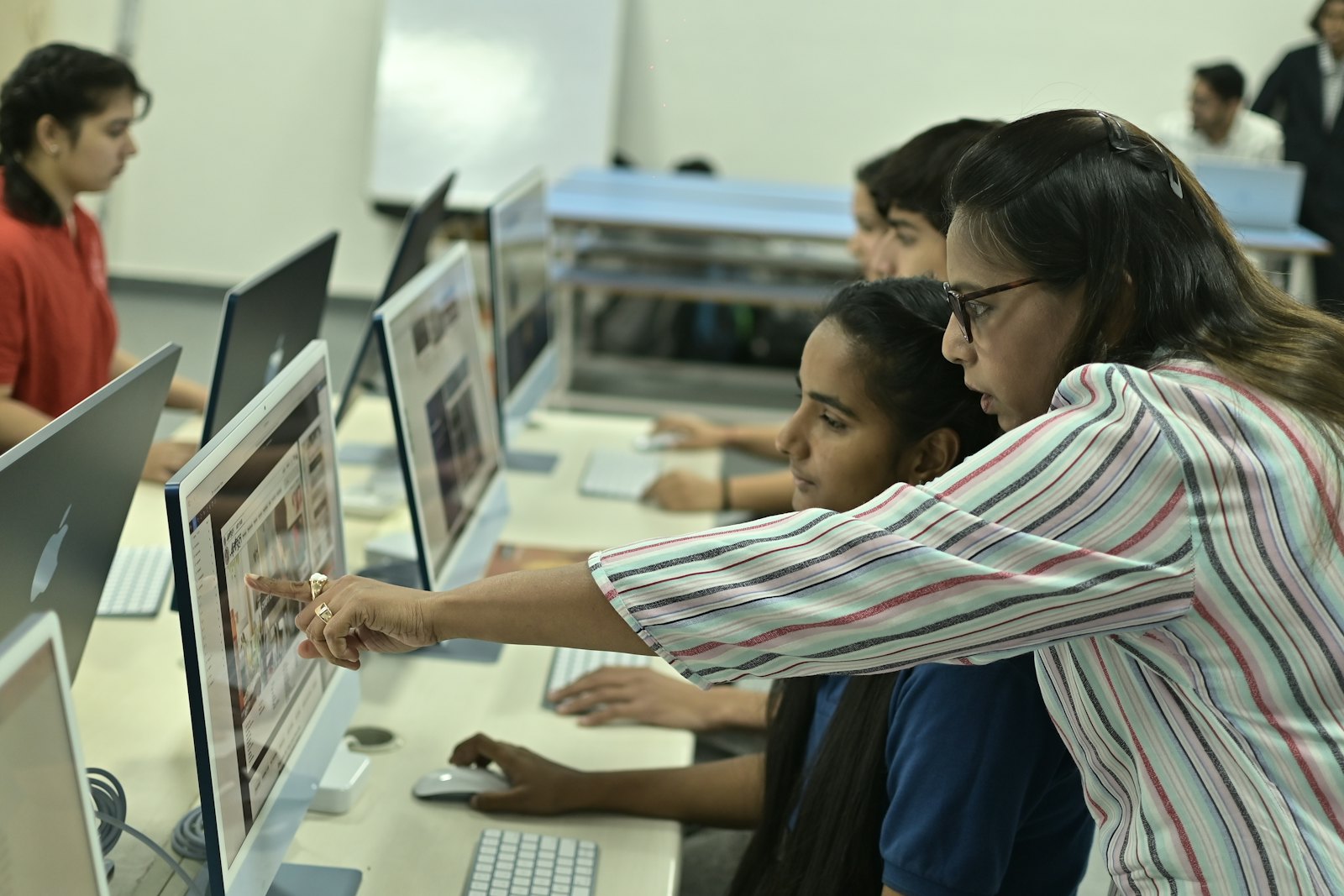 A teacher helping students at computers in a school classroom